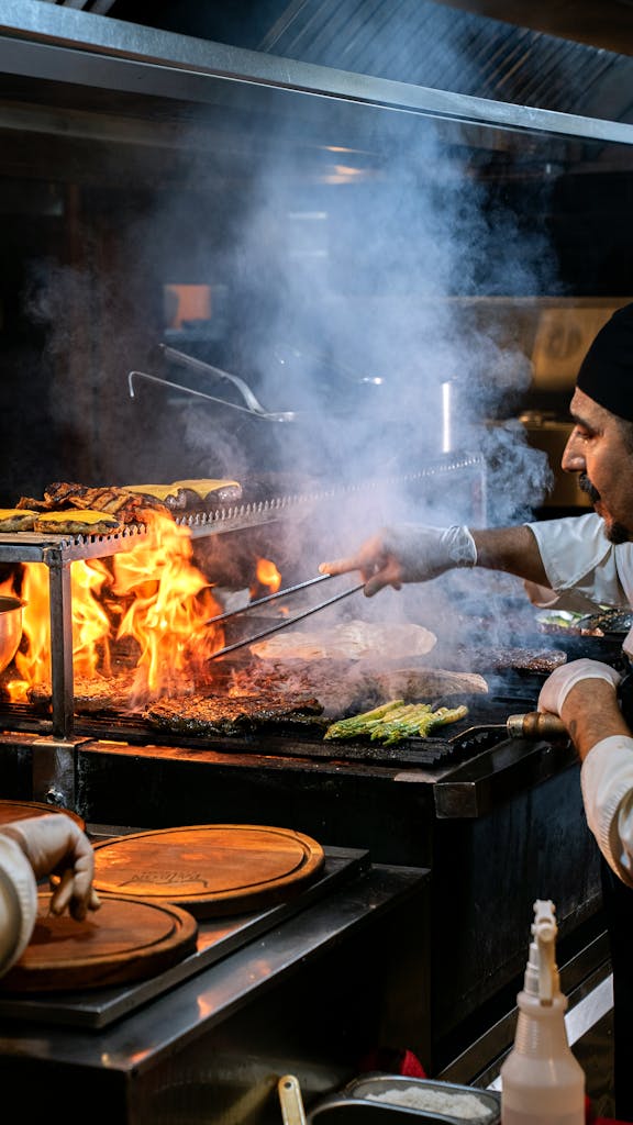 A chef skillfully grills vegetables and meats over an open flame in a bustling restaurant kitchen.