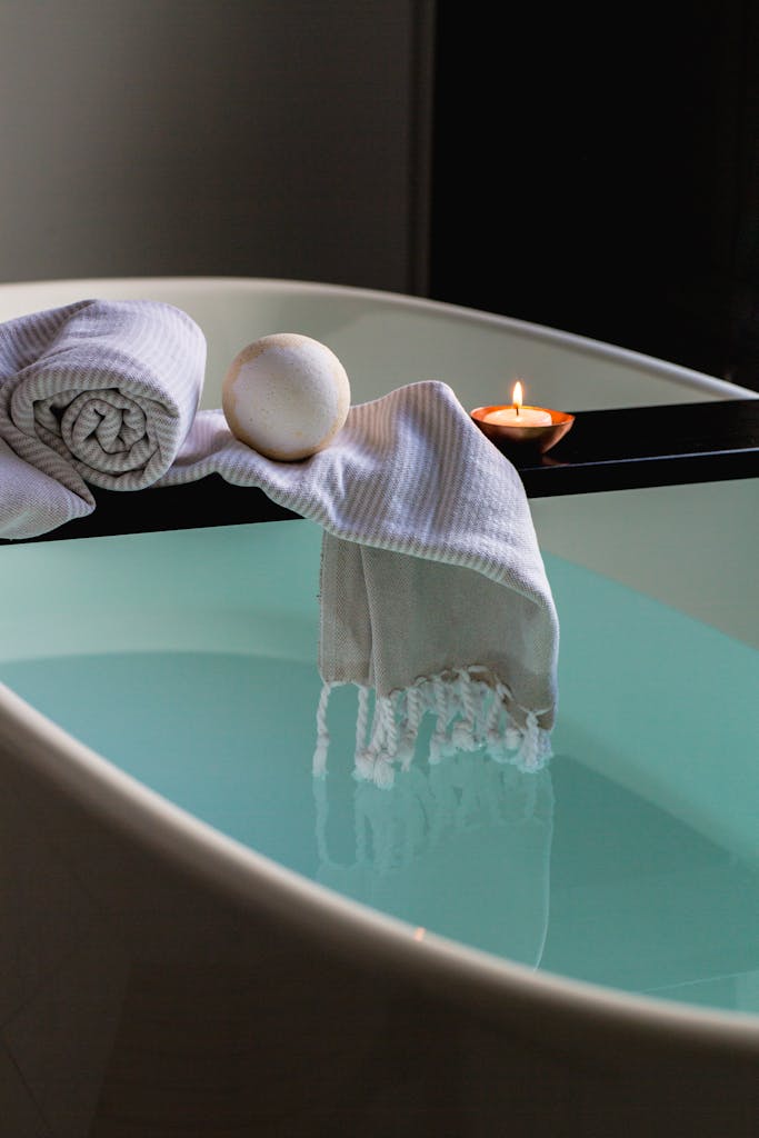 Elegant indoor spa setting with bathtub, candle, towel, and bath bomb for relaxation. spa